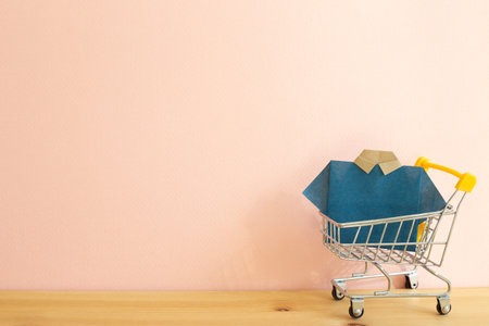 Blue paper shirt origami in shopping cart on wooden table. Pink background, copy space. Clothes shopping conceptの写真素材