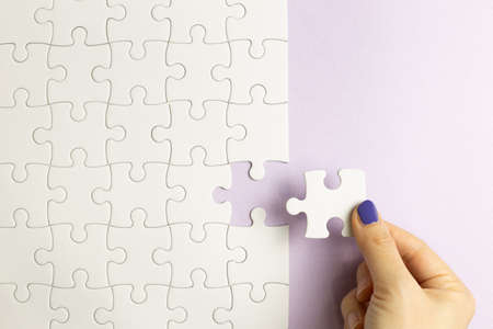 Set of white puzzle pieces and hand holding last one piece on purple background. top viewの写真素材