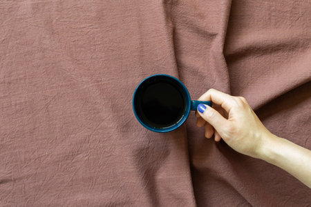Hand holding cup of coffee on brown fabric background. top view