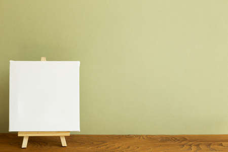 Easel with blank canvas on wooden desk. khaki green background. copy spaceの写真素材