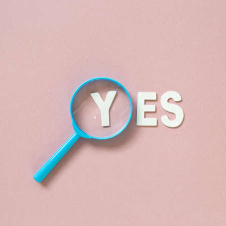 Word'YES' and magnifying glass on pink background. top viewの写真素材