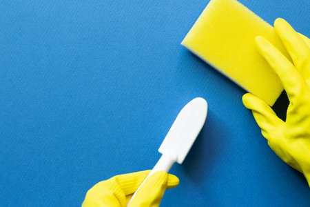 Hand in yellow gloves hold sponge and brush on blue background. Cleaning concept. top view, copy...