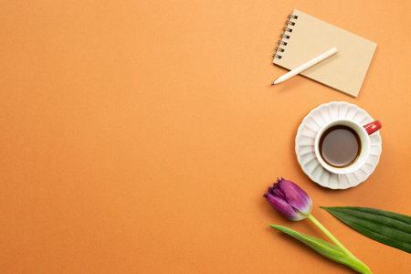 Notebook, pencil, cup of coffee, tulip flower on orange background. Work and study place. flat lay,...