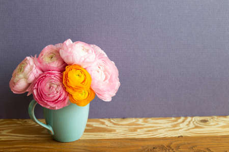 Vase of fresh ranunculus flowers on wooden table. purple backgroundの写真素材