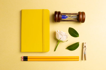 Notebook, sandglass, pencil, clip, rose on yellow gold background. Work and study place. flat lay,...