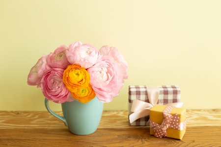 Gift boxes and vase of ranunculus flowers on wooden table. yellow background