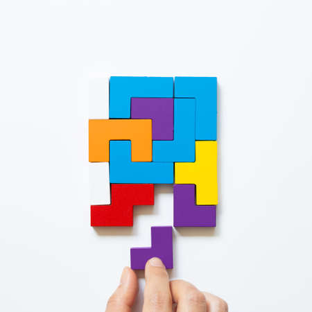 Set of color blocks puzzle pieces and hand holding last one piece on white background. Creative thinking, idea, problem solving, success concept. top viewの写真素材