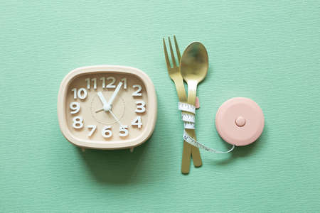 Fork and spoon with measuring tape, clock on green background. Diet conceptの写真素材