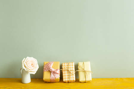 Yellow gift boxes and vase of white rose flower on wooden table. khaki green backgroundの写真素材