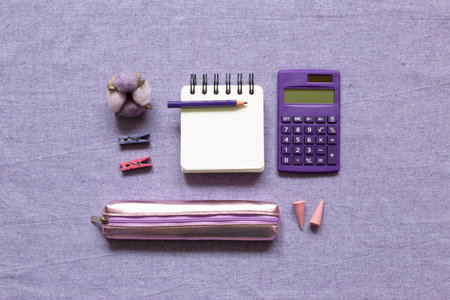 Notepad, colored pencil, calculator, wooden clip, pencil case, candle, cotton plant on purple fabric...