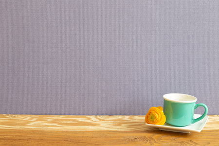 Mint green coffee cup with yellow flower on wooden table. purple background
