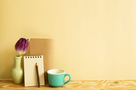 Notebook, colored pencil, tulip flower, mug cup on wooden desk. beige background. Work and study...