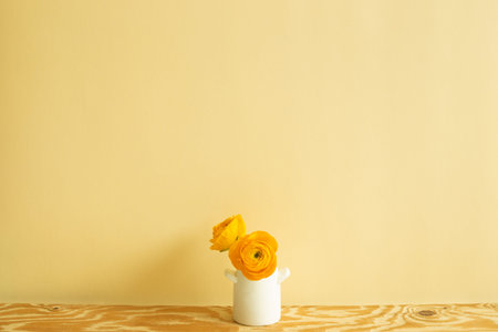 Vase of yellow ranunculus flowers on wooden table. beige background