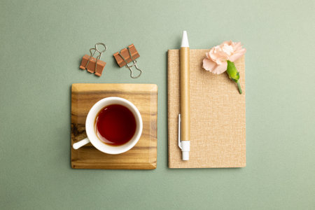 Notebook, cup of tea, clip, pen, carnation flower on green background. flat lay, top view, copy...