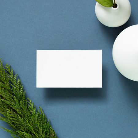 Blank white business card with vase of plant on desk. navy blue background. flat lay, top view, copy...