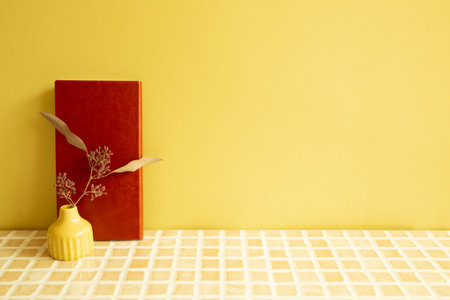 Notebook and vase of dry flowers on beige ceramic mosaic tile desk. yellow wall background. Work and study placeの写真素材