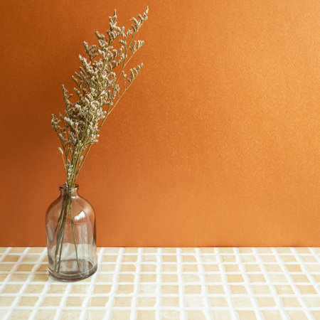Vase of misty blue dry flowers on beige ceramic mosaic tile table. Orange background. home interior