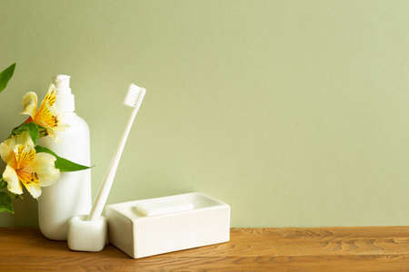 Shampoo bottle, toothbrush, soap, flower on wooden table. khaki green wall background. Bathroom interior. Skin care and spa conceptの写真素材