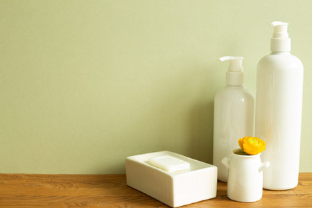 Shampoo bottle, soap, flower on wooden table. khaki green wall background. Bathroom interior. Skin...