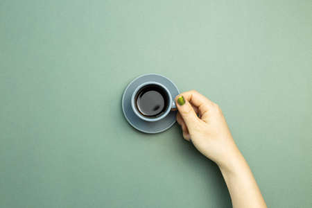 Hand holding cup of coffee on green background. top view, copy spaceの写真素材
