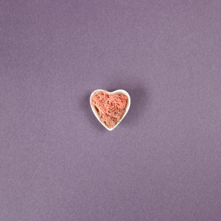 Pink dry moss plant in heart shape vase on purple background. flat lay, top view, copy space