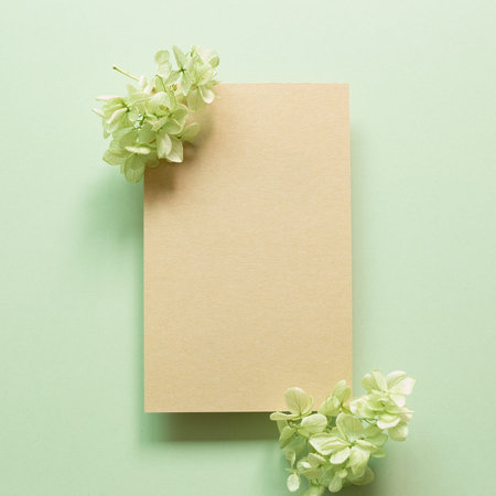Blank kraft memo pad with dry hydrangea flowers on green background. top view, copy space