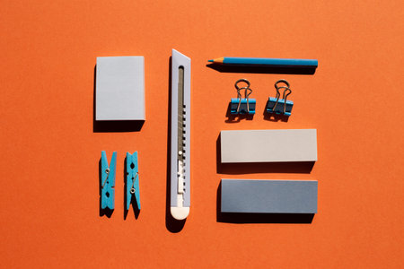 Blue memo notepad, clips, cutter, colored pencil on red background. Work and study place. flat lay,...