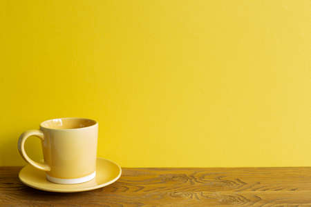 Yellow coffee cup on wooden table. yellow wall background. copy spaceの写真素材