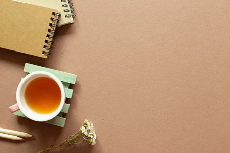 Notebook, colored pencil, dry flower, tea cup on brown background. flat lay, top view, copy space. Work and study placeの写真素材