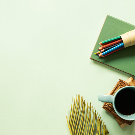 Notebook, colored pencil, coffee, leaf on green background. workspace. top view, copy space