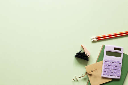 Notebook, calculator, pencil, stapler, eucalyptus leaf on green background. workspace. top view, copy spaceの写真素材