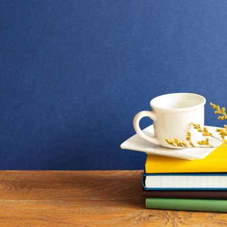Stack of notebooks and coffee cup on wooden desk. blue wall backgroundの写真素材