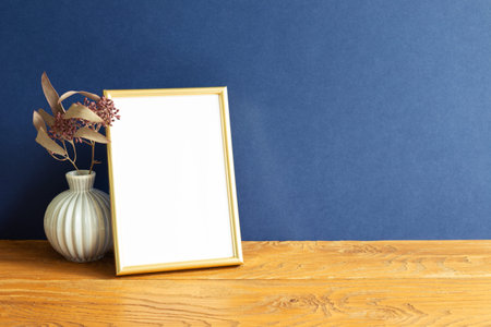 Gold photo frame and dry flowers on wooden table. blue wall background. home interior