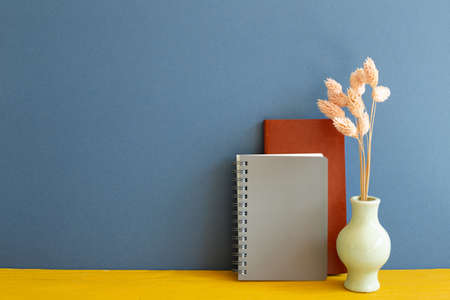 Notebook with dry flowers on yellow wooden desk. blue wall background. copy spaceの写真素材