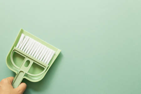 Hand holding green broom and dustpan on green background. Cleaning housework concept. top view, copy spaceの写真素材