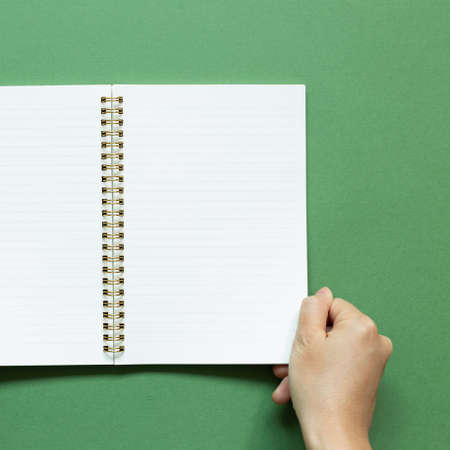 Hand open notebook on green background. top view, copy spaceの写真素材