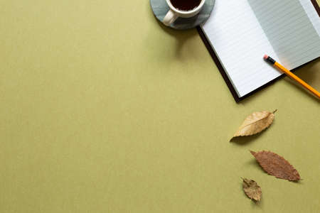 Notebook, cup of coffee, pencil, autumn leaves on khaki background. workspace. flat lay, top view, copy spaceの写真素材