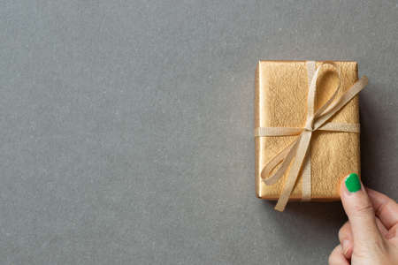 Hand holding gold gift box on gray background. top view, copy spaceの写真素材