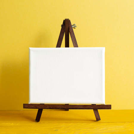 Easel with blank canvas on wooden table. yellow wall backgroundの写真素材