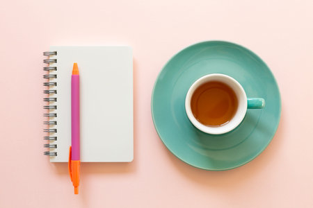 Blank notepad and cup of tea on pink background. workspace. top view