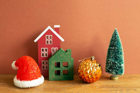 Winter christmas concept. Santa claus hat, house model, bauble, tree on wooden table. red brown backgroundの写真素材