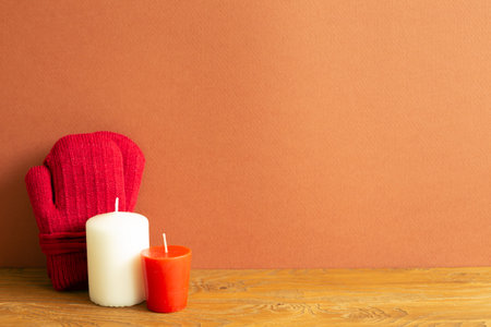 Winter gloves and candles on wooden table. red brown background. copy space
