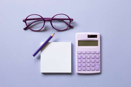 Notepad, colored pencil, calculator, glasses on purple background. workspace. flat lay, top viewの写真素材