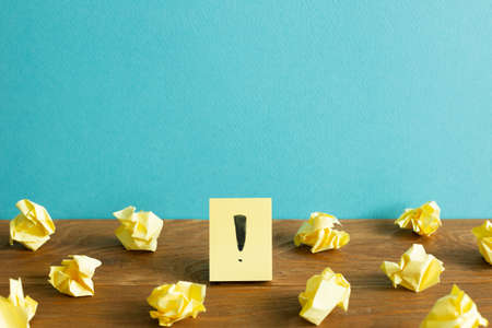 Crumpled paper balls and notepad with exclamation mark on wooden desk. blue wall background. Thinking, solution, business, idea conceptの写真素材