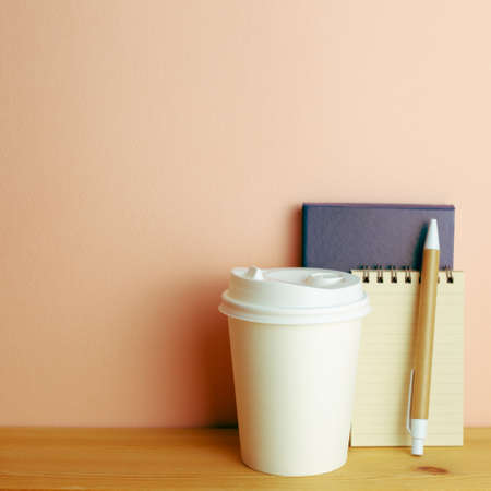 Notebook, pen, paper coffee cup on wooden desk. pink wall background. workspaceの写真素材