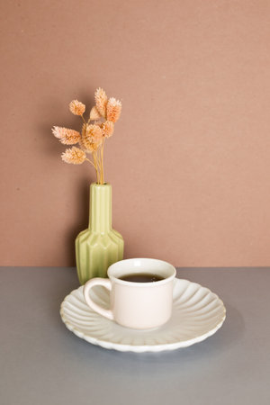 Cup of tea and vase of pink dry plant on gray table. brown wall background