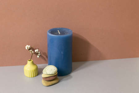 Navy candle and stack of pebble stones and dry plant on gray table. brown wall background. home decorの写真素材