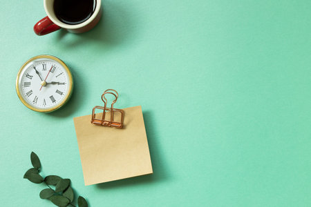 Notepad, clock, cup of coffee, green leaf on mint green background. office desk, workspace. top view