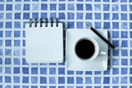 Blank white notepad and cup of coffee on blue ceramic mosaic table. top view, copy spaceの写真素材