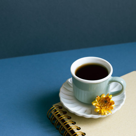 Notebook and cup of coffee on desk. navy blue wall background. workspace